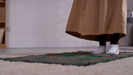 Close-Up-Of-Muslim-Woman-At-Home-Laying-Down-And-Standing-On-Prayer-Mat-On-Floor